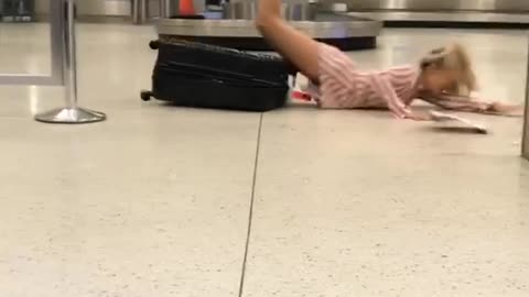 Girl in airport balancing on luggage falls on stomach