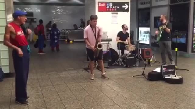 Guy in pink shirt plays saxophone in a subway station