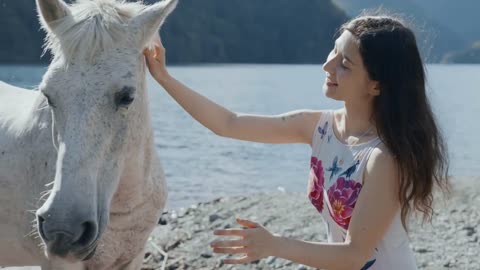 Pregnant woman petting white horse by the mountain lake at beautiful sunlight