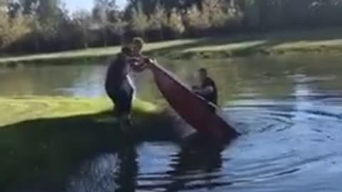 Two guys flip friend inside of red boat into lake