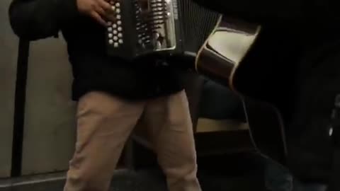 Guy on subway plays accordion and gives thumbs up to camera