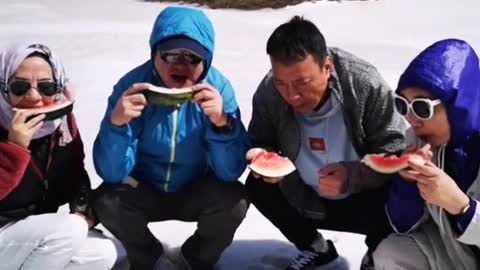 A group of people eating watermelon in a snow day!