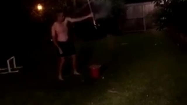 Shirtless guy in a backyard sets off fireworks