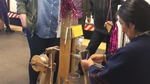 Crowed standing around woman weaving bracelets subway