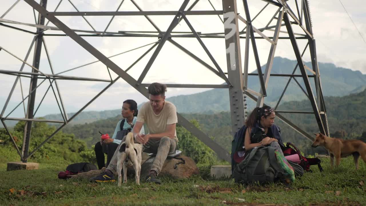 Campers sitting on the rocks under a tower at the mountain, playing with dogs