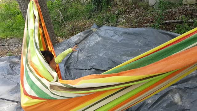 The two children are laughing and playing in the hammock.