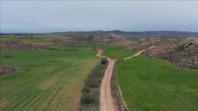 dirt road aerial shot between green fields pasture spain cloudy day