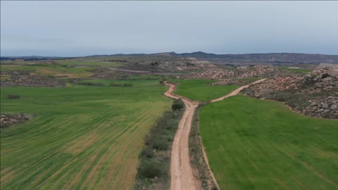 dirt road aerial shot between green fields pasture spain cloudy day