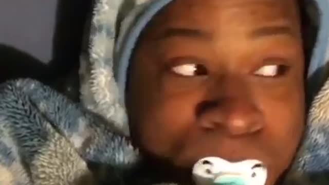 Guy with pacifier on bed covered in blanket