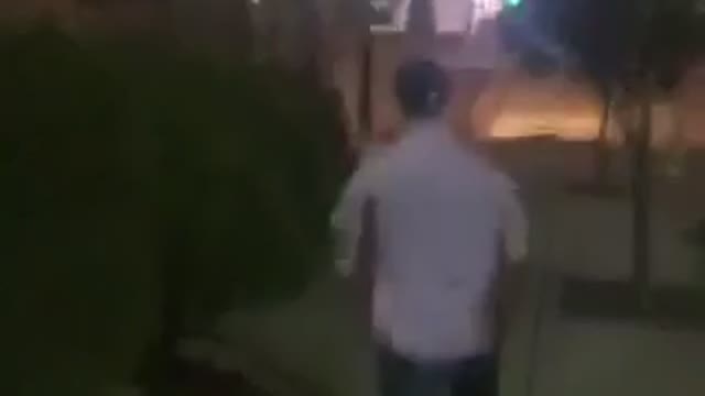 Man in button down shirt runs down sidewalk and dives into bush