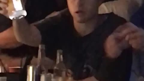 Guy at bar holding drink and waving it