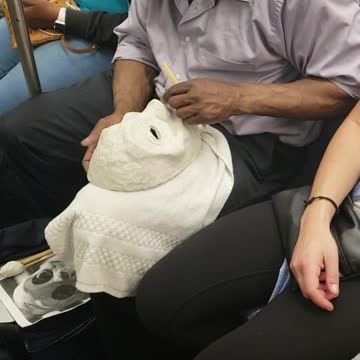 Man on subway train carving a white mask