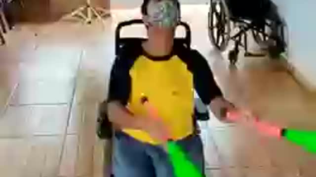 Guy in Wheelchair Balances One Baton on Forehead While Juggling Three Other Batons