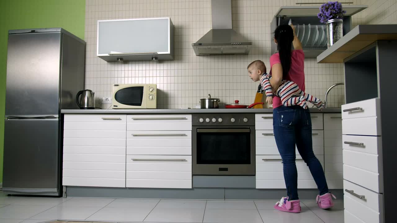 Young woman cooking in a kitchen carrying her baby