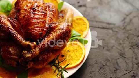 Roasted whole chicken or turkey served in white ceramic plate with oranges