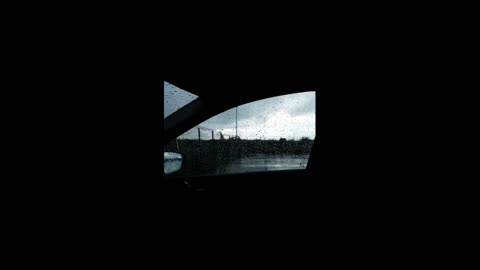 I sit in the car and outside the window the rain is drumming