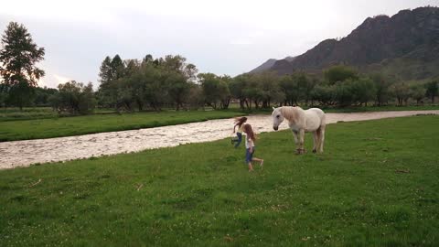 two little girls running around the lawn around horses