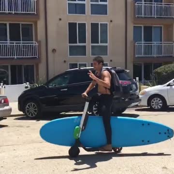 Guy on electric scooter carrying blue surf board
