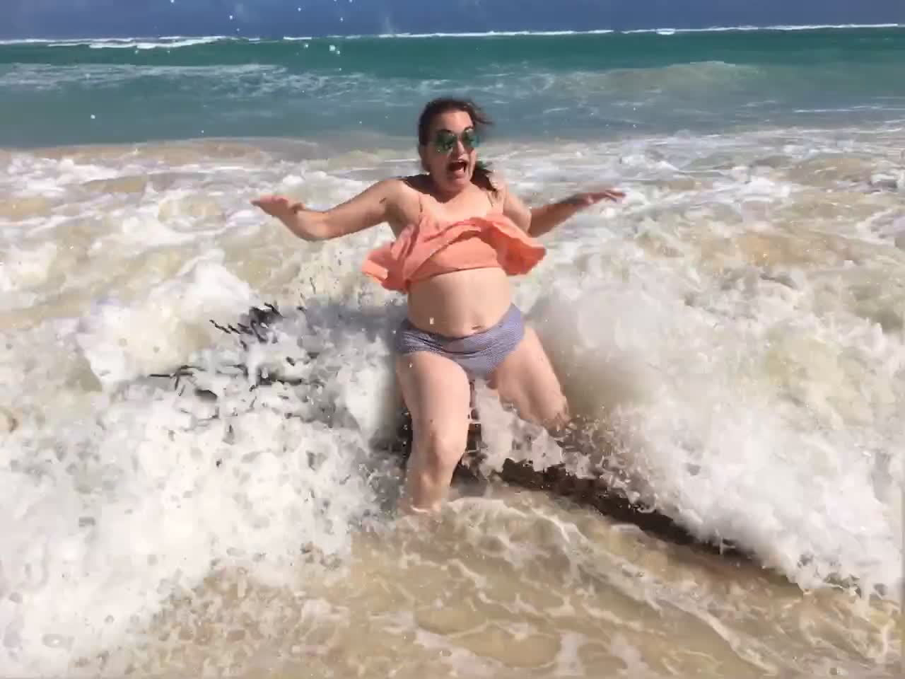 Girl sitting on tree branch beach water gets knocked forward by wave