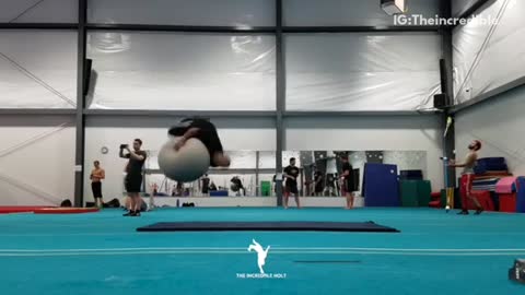 Shirtless guy and black shirt guy do backflips on exercise ball