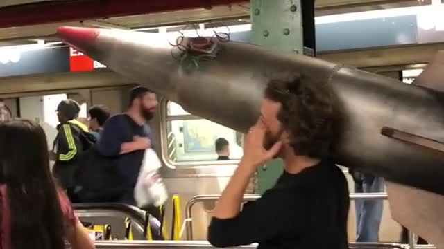 Man carrying large fake missile through subway