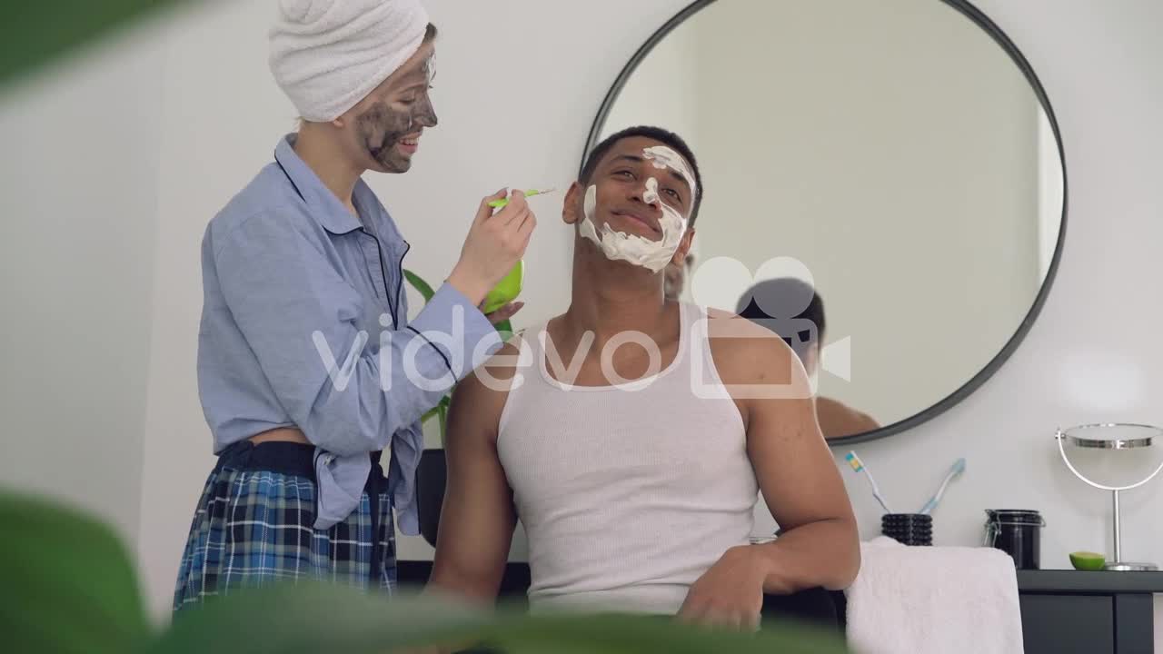 Woman With Facial Mask Applying Scrub To A Handsome Black Man