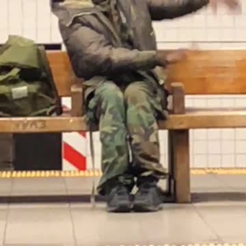 Camo dressed guy sitting on bench waving arms