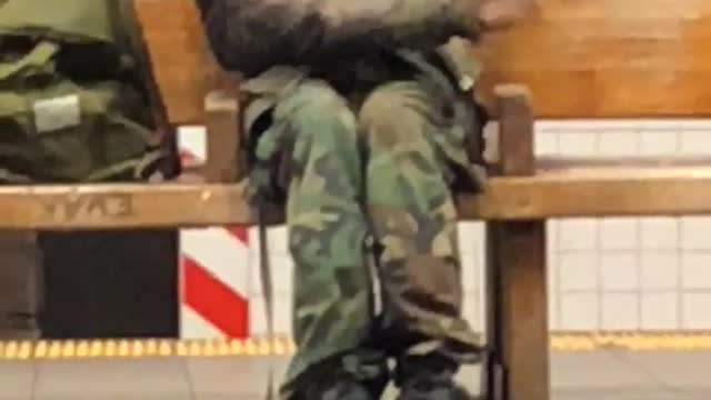 Camo dressed guy sitting on bench waving arms