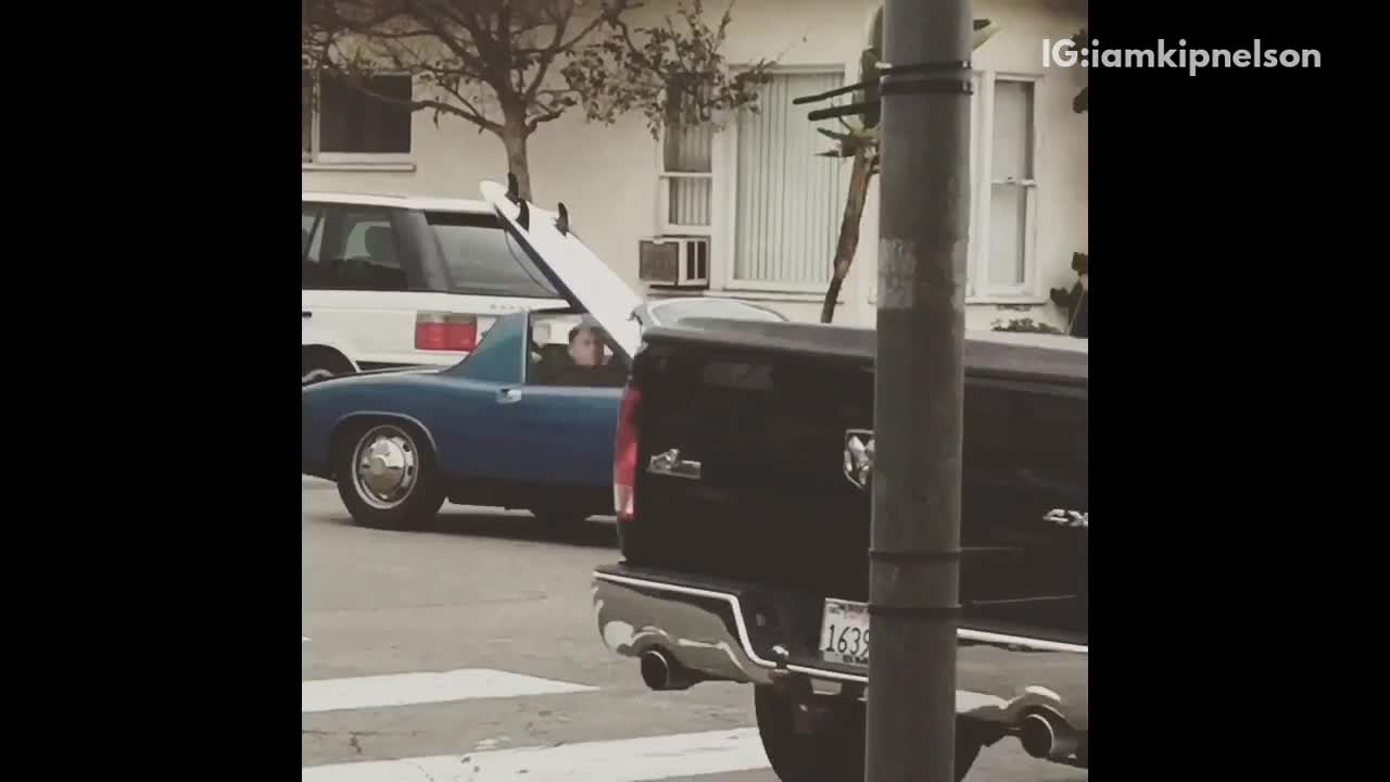 Blue convertible car drives around with white surfboard in it