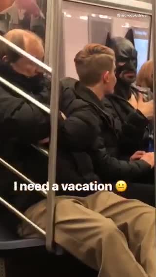 Man wearing batman mask costume casually talks to subway passenger