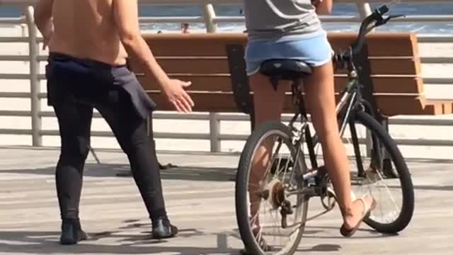 Older man in wetsuit standing next to young girl on a bike
