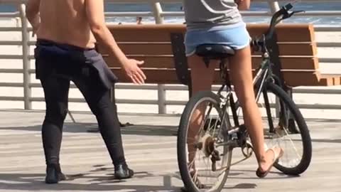 Older man in wetsuit standing next to young girl on a bike