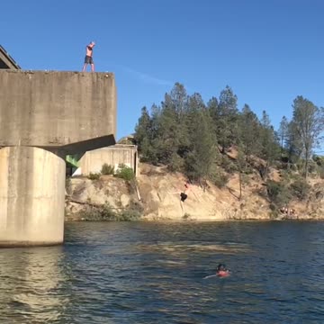 Two guys on bridge back flip into water