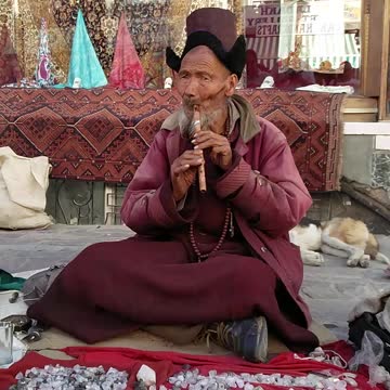 A tribal man in traditional attire playing flute in Leh Market, Leh, Jammu and Kashmir, India