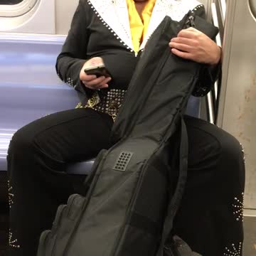 Man with elvis costume carrying large instrument case