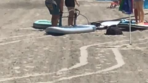 People blowing up inflatable surf board on beach