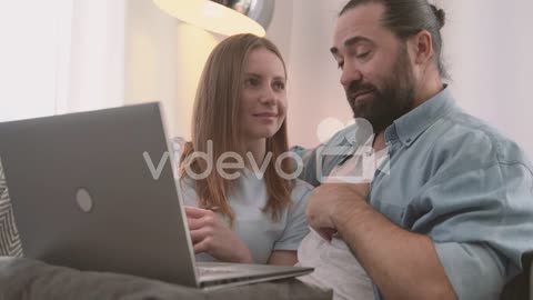 A Happy Couple Have A Relaxed Conversation Sitting On The Sofa And Looking At The Laptop 1