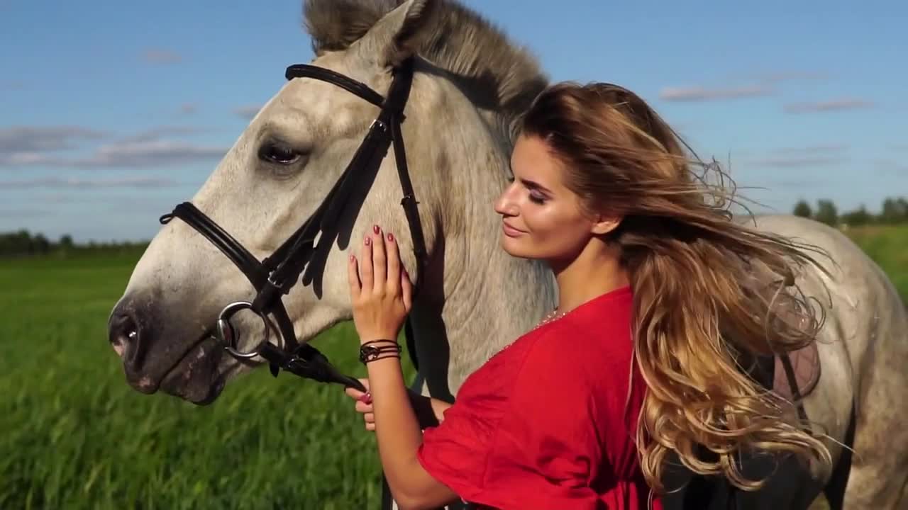 Portrait of young beautiful woman dreesed in red with white horse near the field