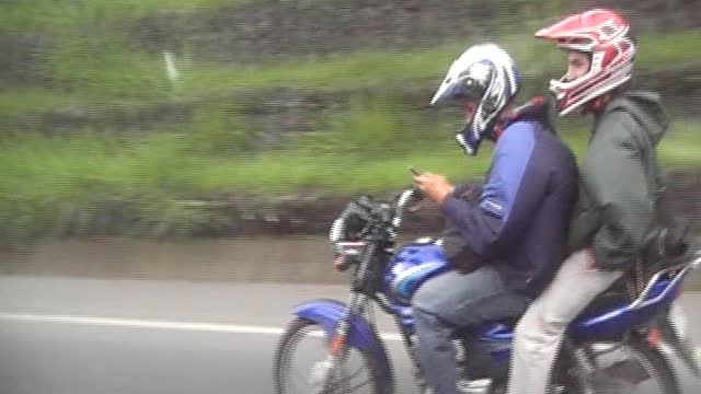 Costa Rica Kid on Motorcycle with friend on back is texting as he drives.