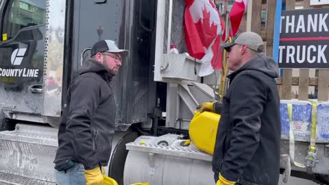 Two gentleman help refill a truck that is directly in front of the Parliament building in Ottawa