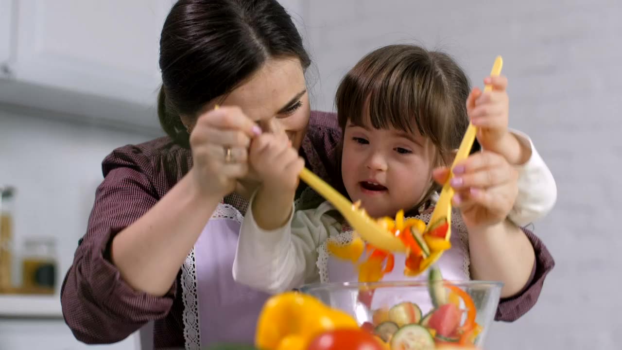 Mother and her lovely daughter mixing a salad together