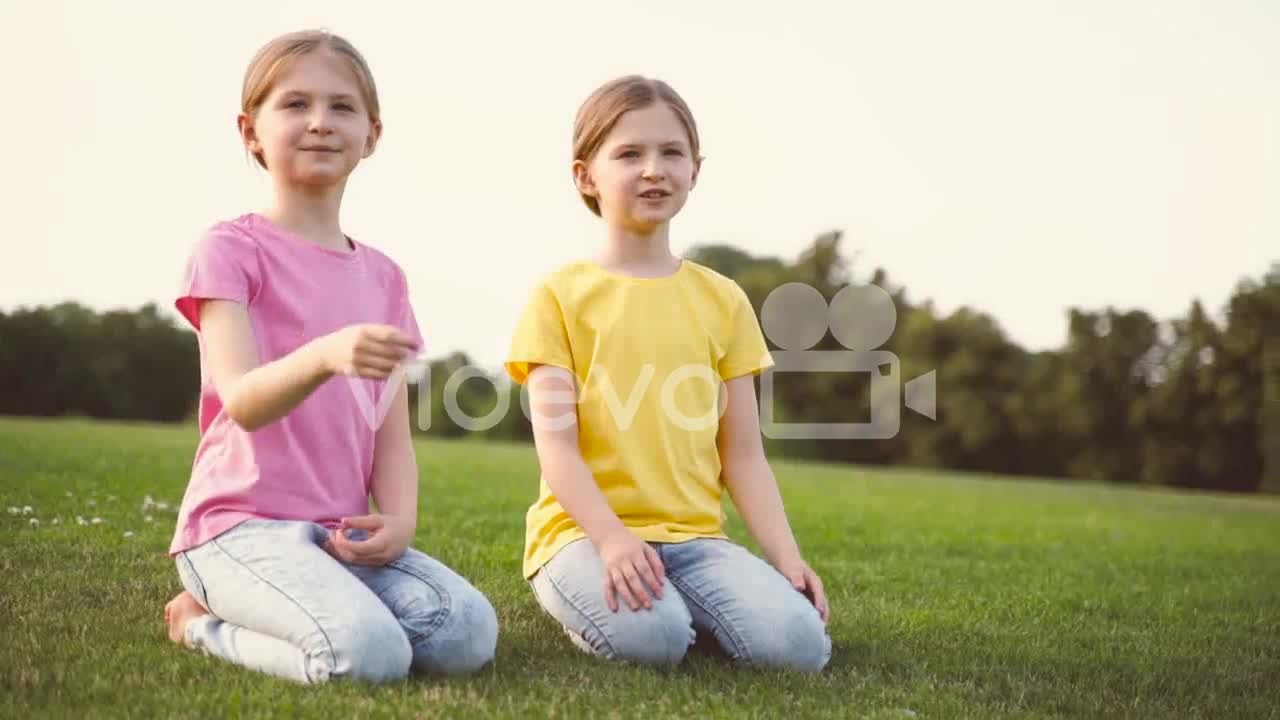 Two Pretty Little Sisters Talking Together, Looking Around And Pointing Something While Kneeling On