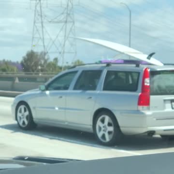 Grey silver car carrying white surf board