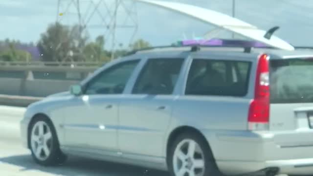 Grey silver car carrying white surf board