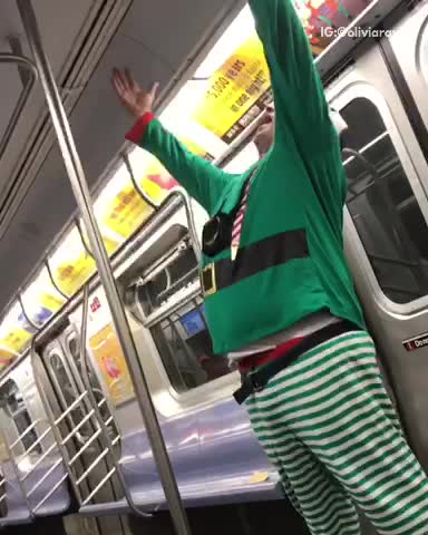 Guy in green elf costume with blue hat singing through microphone speaker