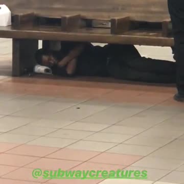 Guy in all black sleeping under bench subway underground
