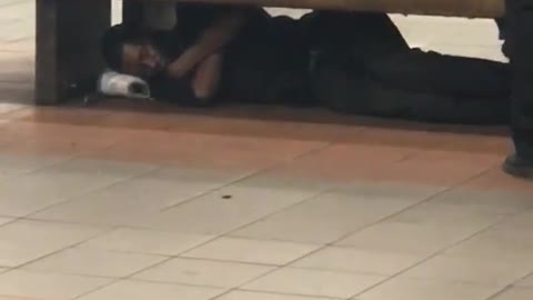 Guy in all black sleeping under bench subway underground