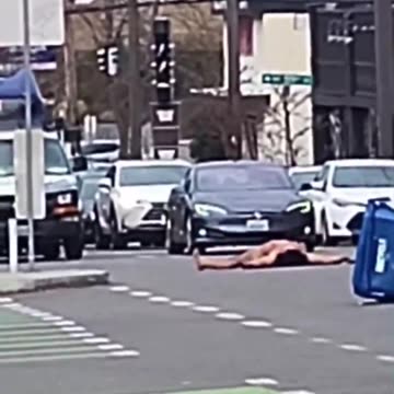 naked Trans activist covered in an LGBTQI+ flag blocks traffic in Seattle