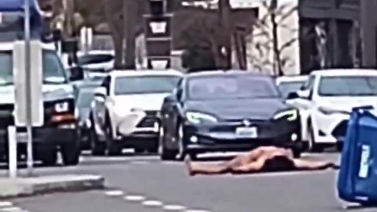 naked Trans activist covered in an LGBTQI+ flag blocks traffic in Seattle