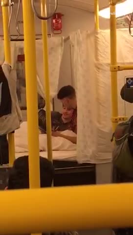 Two guys set up a bed and tarps in a subway train, reading book